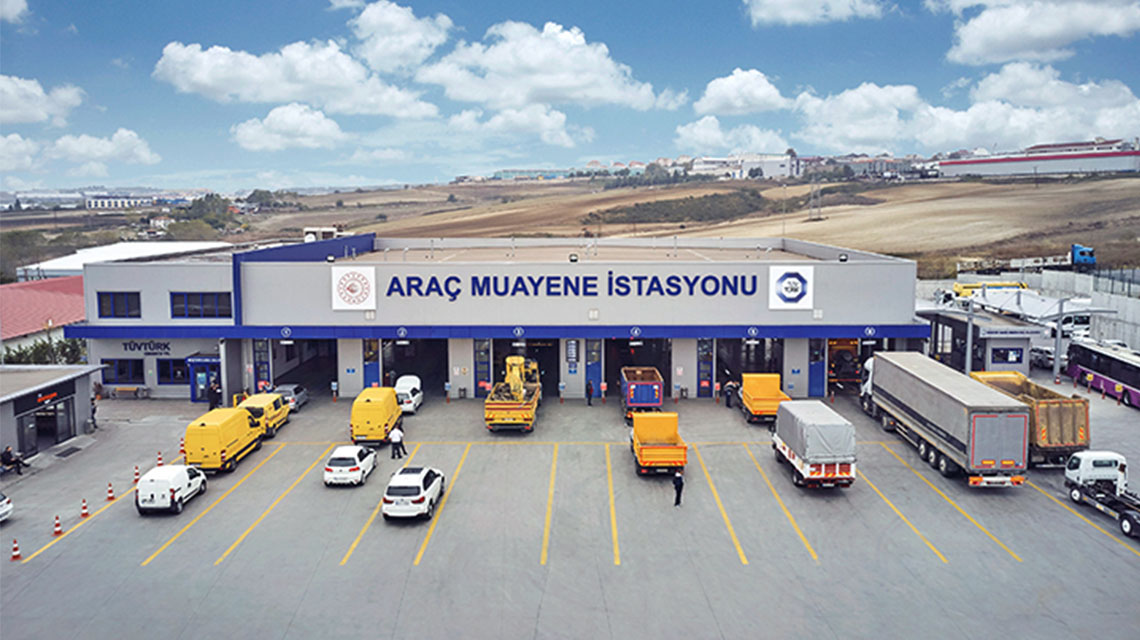 Multiple vehicles, including trucks and vans, are lined up in front of inspection bays at a large vehicle inspection station.