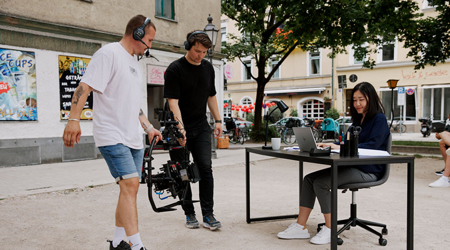 An Asian woman is filmed by two cameramen in an urban environment.