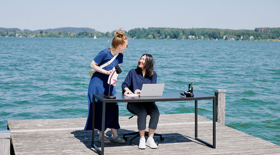 Two women have a laugh together on a pier at a Bavarian lake.