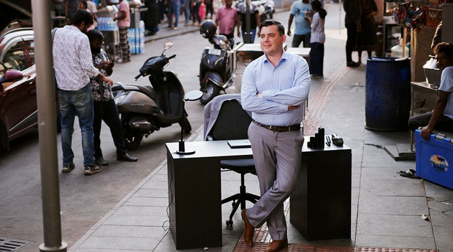 A man stands in front of a desk on a busy street in India