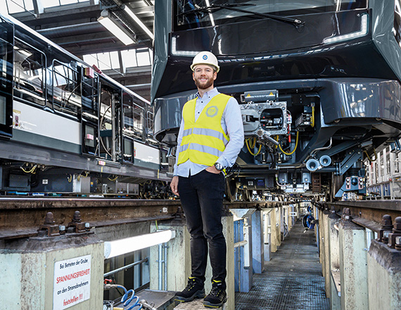A man wearing a yellow high-visibility waistcoat and helmet stands in front of a train at a test station.