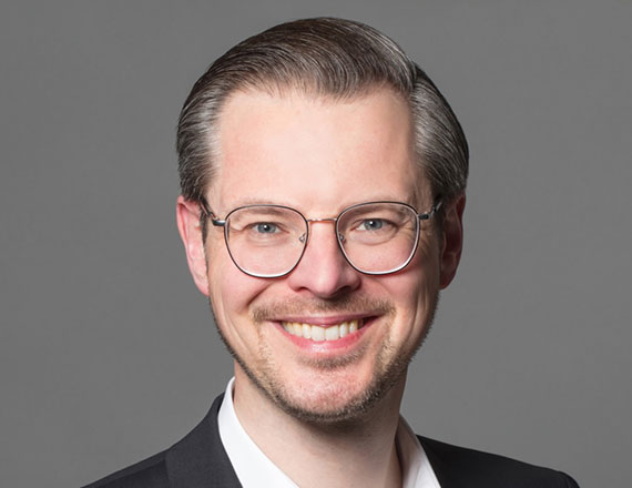 Florian Wilken, Director Data Analytics & AI at TÜV SÜD, is wearing a dark suit and a white shirt, smiling into the camera.