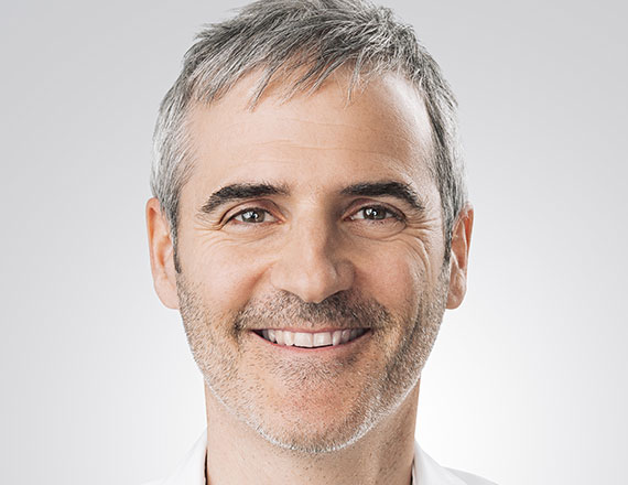 Philippe Coution, Director Digital Interaction & Automation at TÜV SÜD, is wearing a white shirt, smiling into the camera.