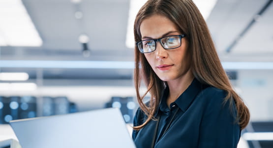 Frau mit langen, braunen Haaren und Brille blickt auf Laptop: Symbolbild für Schulungen