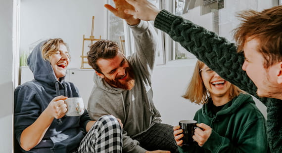 Vier lachende, junge Menschen, die in einer Kuch Kaffee trinken