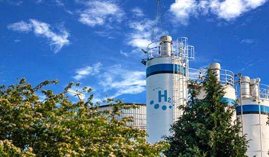 Mehrere Wasserstofftanks umgeben von Bäumen vor blauem Himmel