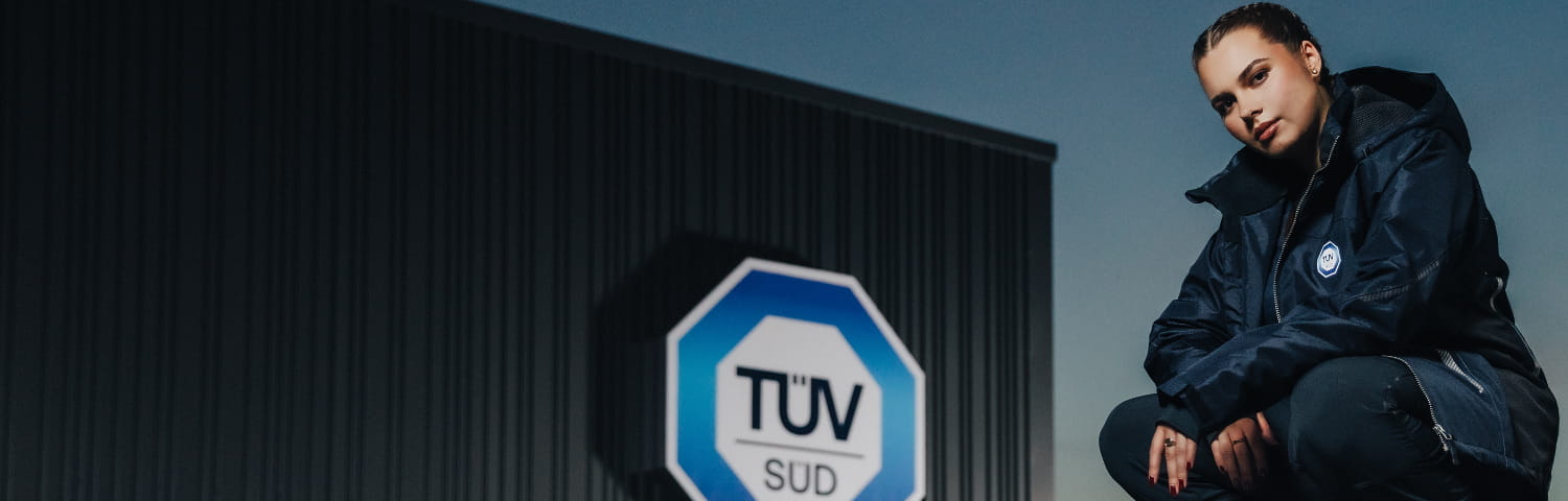 Hockende Frau in dunkler Kleidung mit TÜV SÜD-Logo im Hintergrund