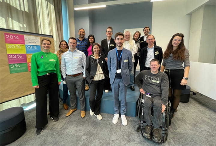 Eine vielfältige Gruppe von Menschen steht in einem Konferenzraum und lächelt in die Kamera.