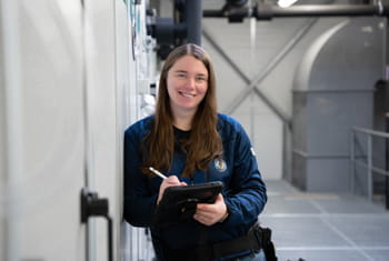 Frau steht mit Tablet in der Hand im Technikraum eines Gebäudes.