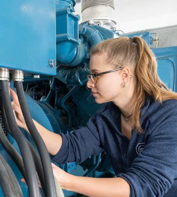 Technikerin inspiziert industrielle Maschinen in einem technischen Umfeld.