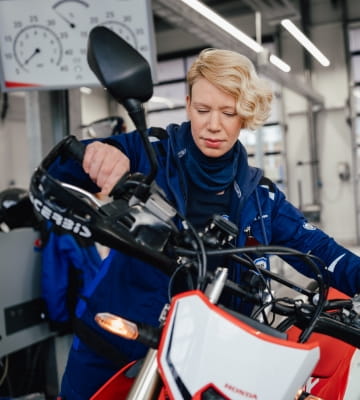 Mitarbeiterin in Arbeitskleidung prüft ein Motorrad