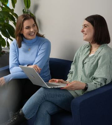 Zwei junge Frauen arbeiten gemeinsam an einem Laptop im Büro.