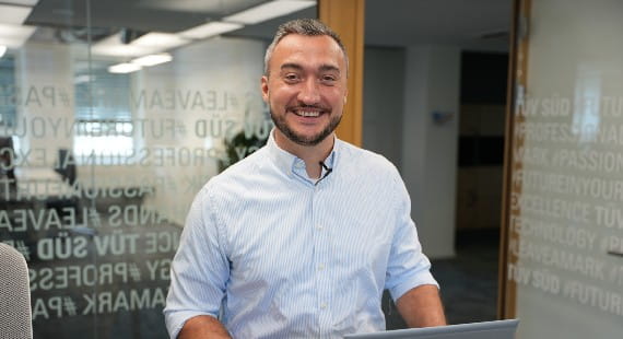 Ein freundlicher TÜV SÜD Büro-Mitarbeiter lächelt fröhlich in die Kamera