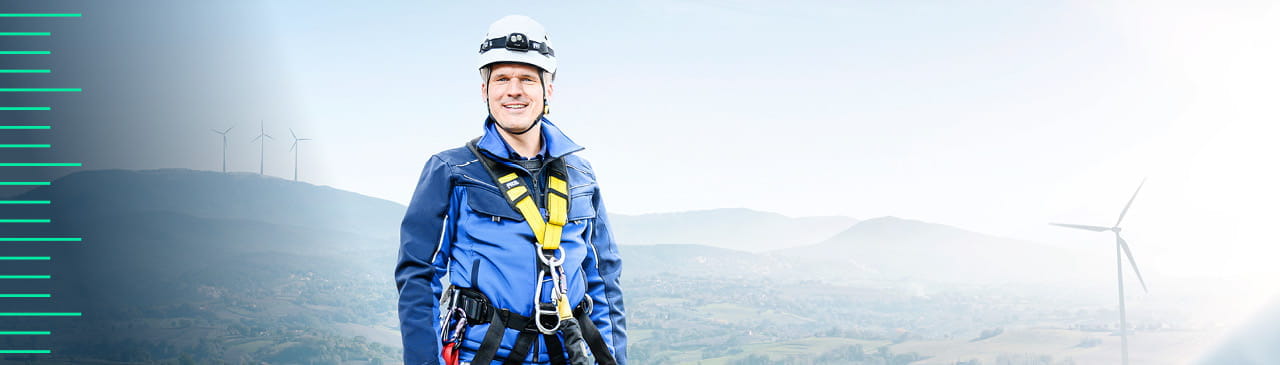 TÜV SÜD Brand - Engineer in safety gear with wind turbines in the background.