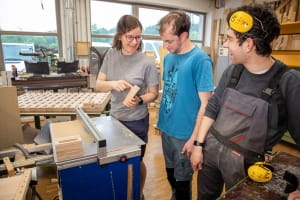Drei Mitarbeitende arbeiten an einem Holzstück in der Schreinerei.