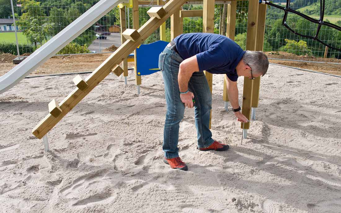 Spielplatzprüfer prüft Untergrund von Spielplatz