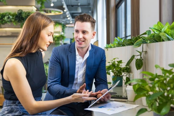 Zwei Kolleg:innen im Gespräch mit Tablet und Diagrammen in modernem Büro