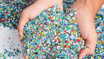 Zwei Hände halten kleine, bunte Plastikteilchen