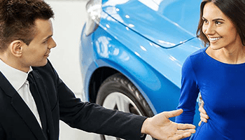 Ein Mann und eine Frau schütteln sich die Hände vor einem blauen Auto