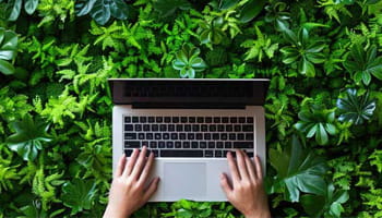 mani che digitano su tastiera computer, con sfondo verde di piante