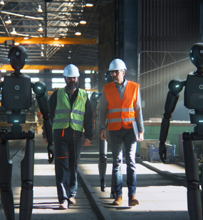 2 Arbeiter mit Warnwesten und Helm und 2 lebensgro&szlig;e Roboter