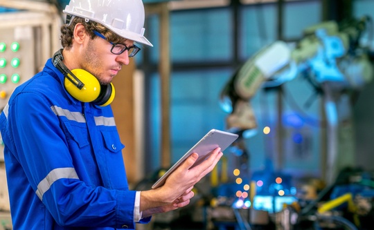 Mann mit Helm und Tablet an einer Maschine