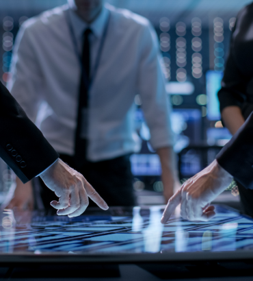 Persone in abiti formali usano uno schermo touch in una sala tecnologica, suggerendo analisi dati o decisioni strategiche.