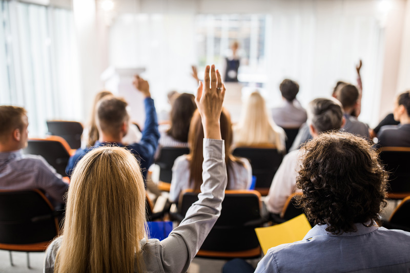 Gruppo di persone dentro un'aula di formazione che alzano la mano